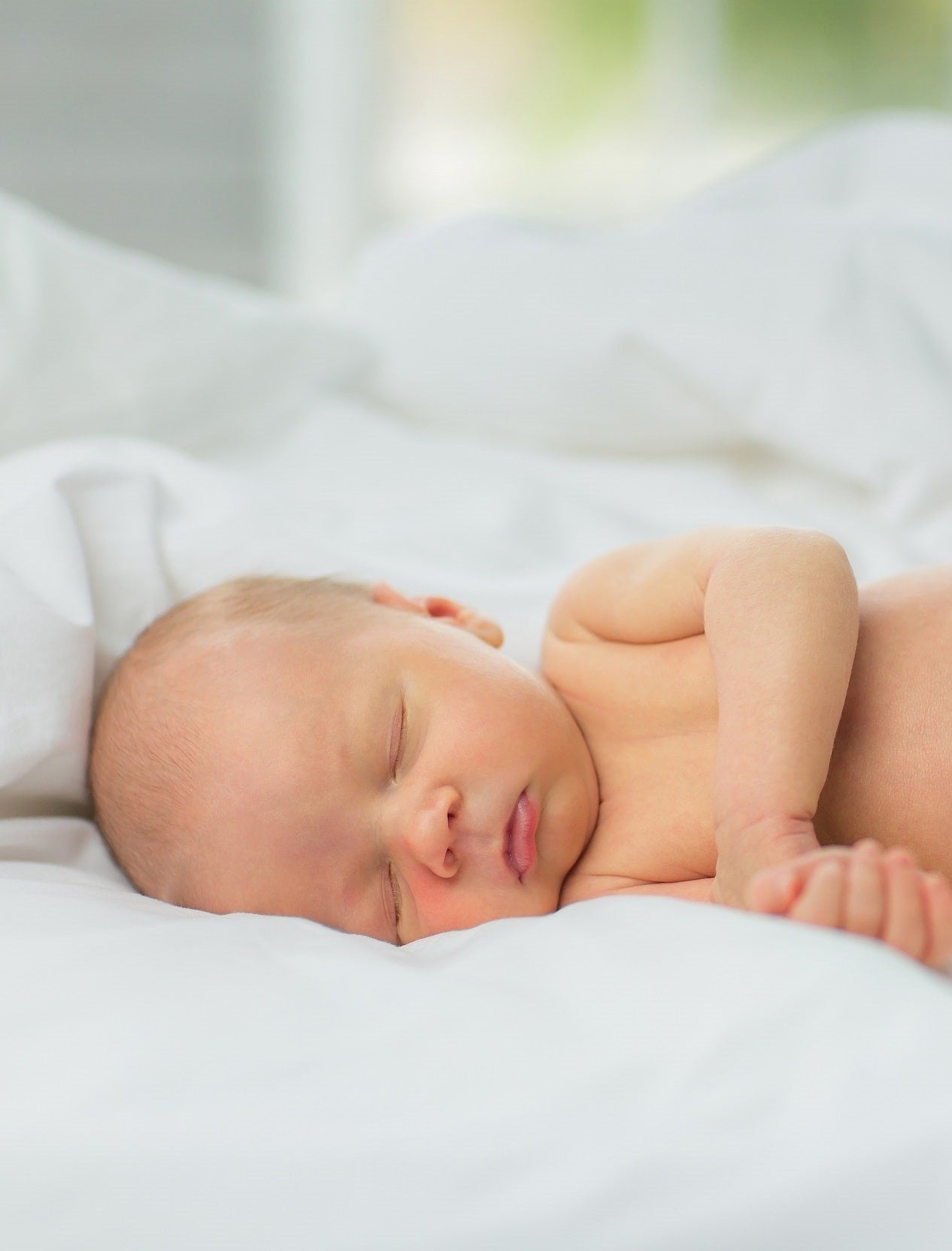 A newborn baby sleeps in white Tencel lyocell sheets.