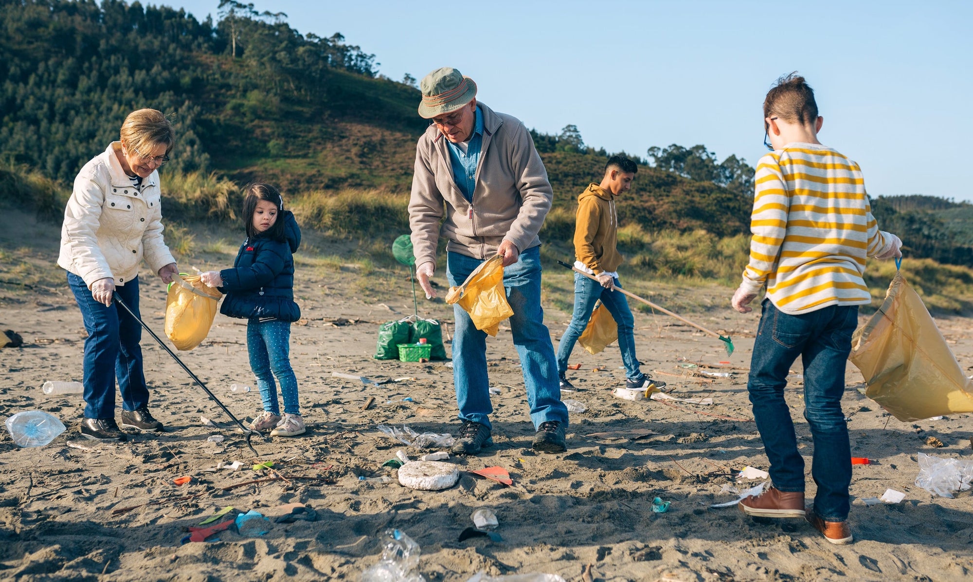 A group of young and old community volunteers are picking up trash on a beach.