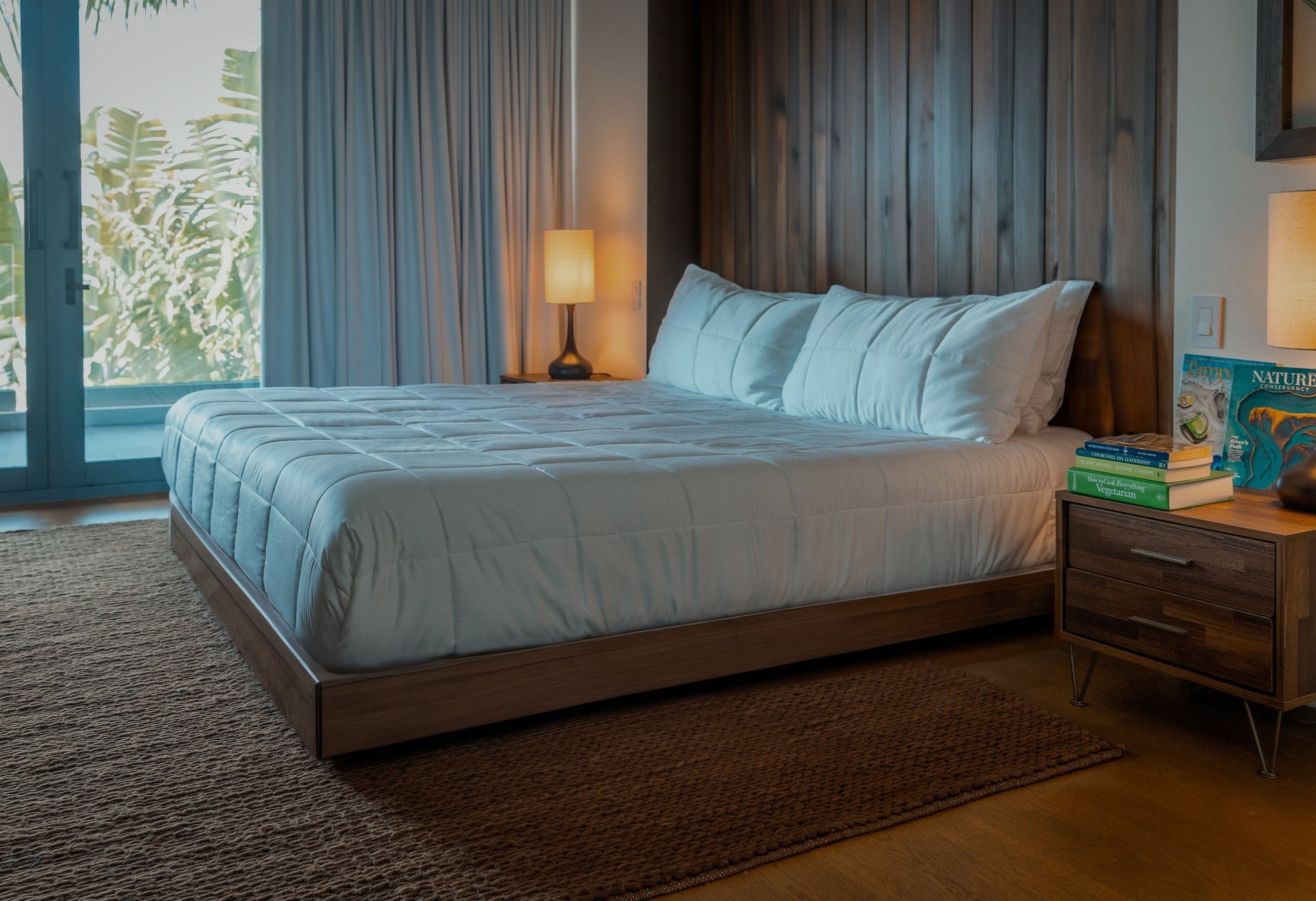 A perfectly made bed with eco-friendly bedding in a sustainably built modern home as the sun is going down.