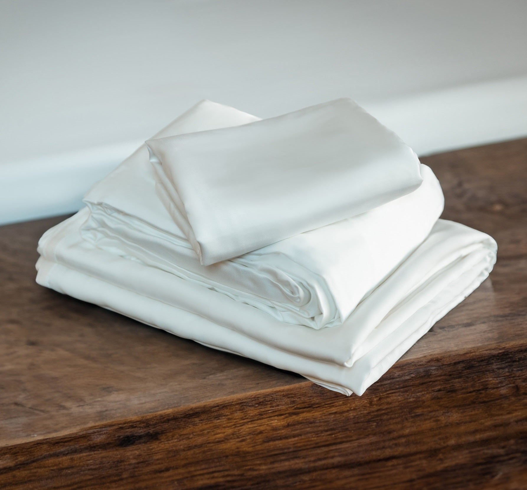 A stack of nicely folded, freshly-washed TENCEL Lyocell bed sheets sits on a wooden end bed table.