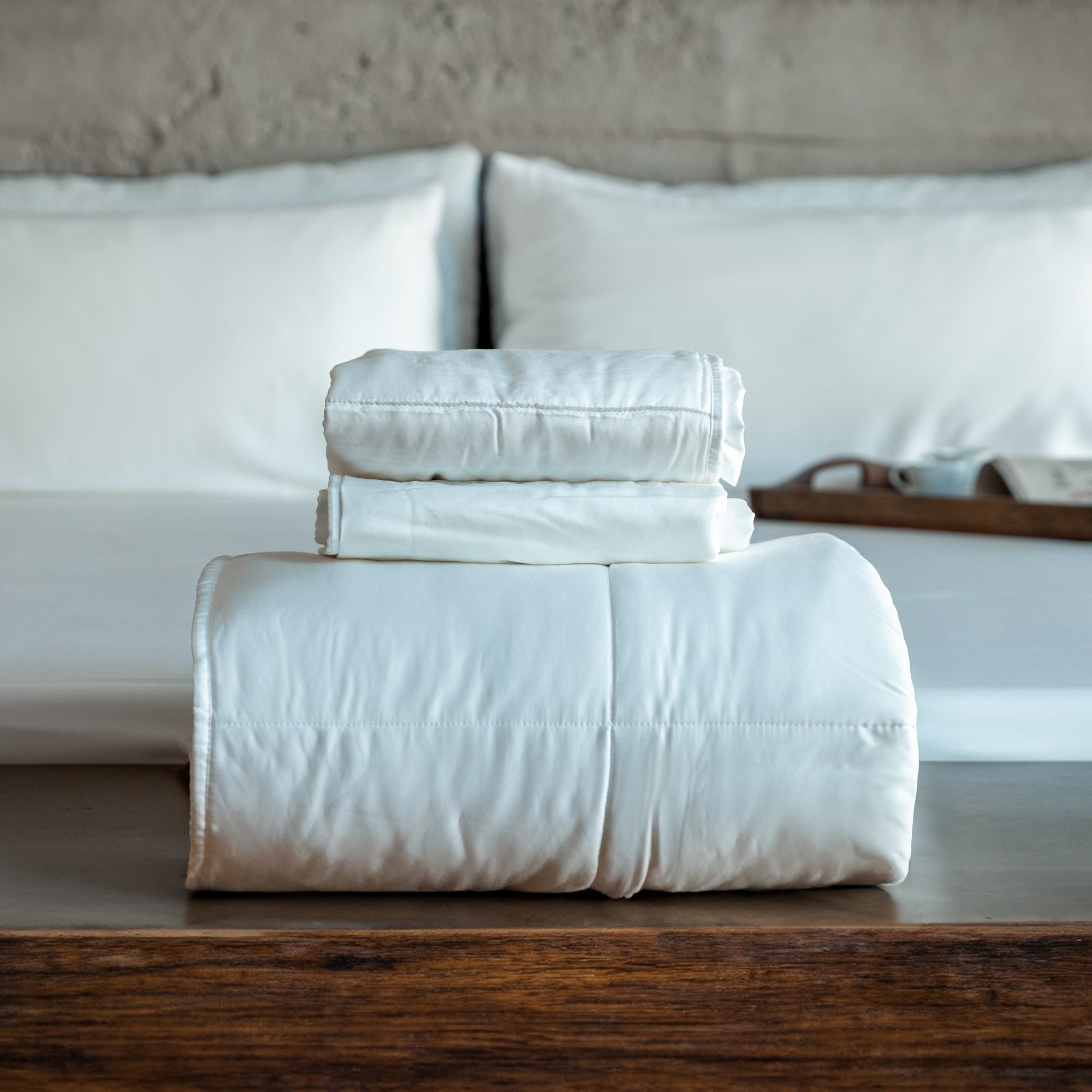 Sleepmod sustainable bedding products are stacked at the foot of a bed on a wooden table in a contemporary eco-friendly house.