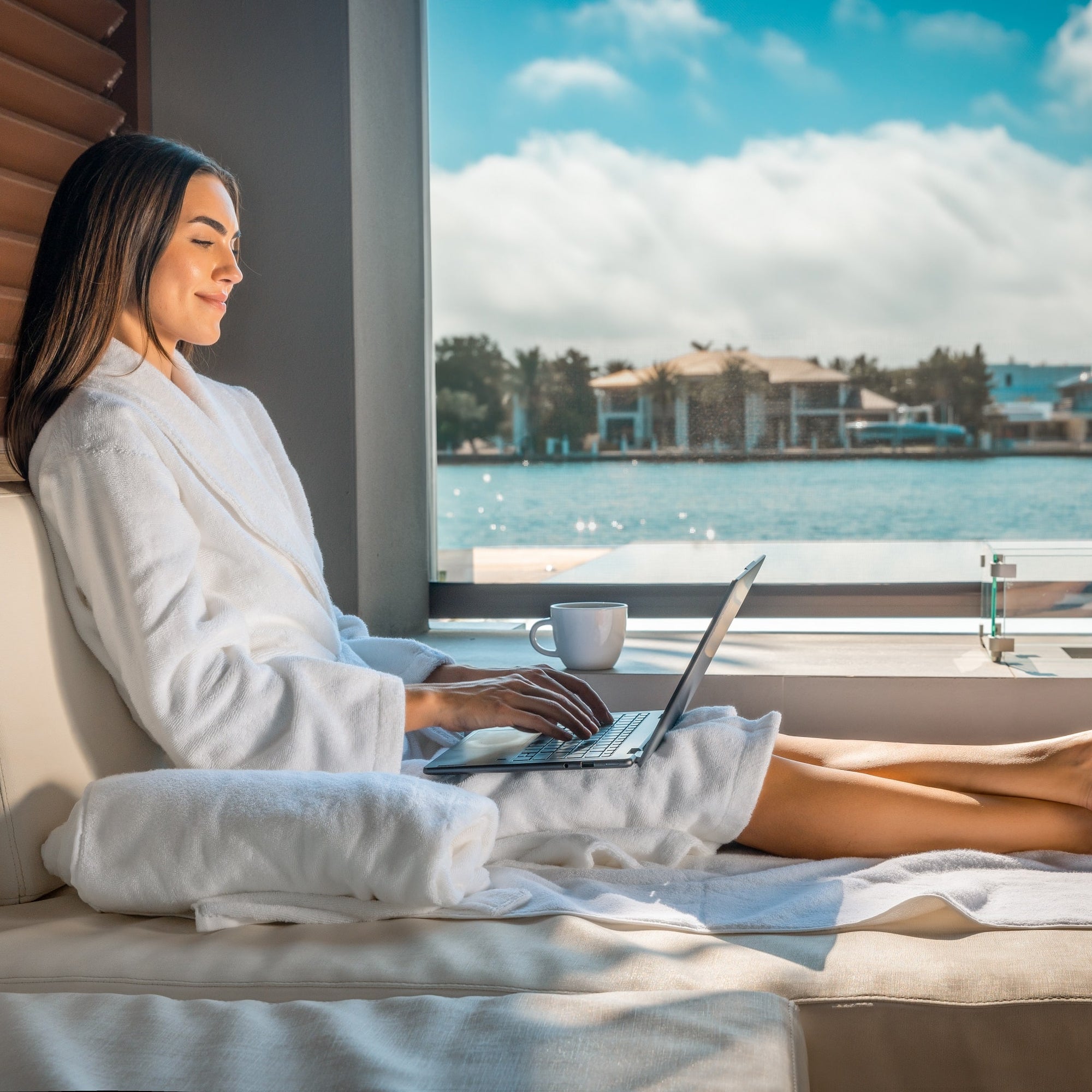 A woman sits by the pool at an eco-spa and hotel working on her laptop.